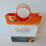 Tapered custom paper bag with high-saturation printing and orange circular piped handles.
