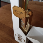 White textured box featuring a gold-foiled acrylic emblem and double-hinged opening.