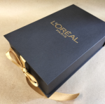 Black hinged lid box featuring a gold ribbon closure and gold foiling.