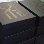 Stacked large-format black rigid boxes featuring tonal black silkscreened branding.