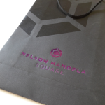 Black matte-finish paper bag featuring a purple foil-stamped logo