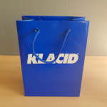 Vibrant blue gloss-laminated paper bag with matching blue braided rope handles and bold white typography.