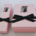 Pink rigid boxes in two sizes featuring a black graphic logo and stitched black ribbon accents.