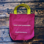 Magenta fabric tote bag with yellow handles and white silkscreened text.