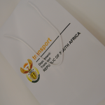 White matte-finish paper bag with white rope handles and full-color departmental crest