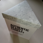Triangle-shaped rigid box featuring a textured marble-patterned lid and minimalist typography.
