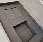 High-angle view of a grey rigid box with custom die-cut board recesses.