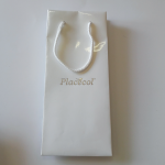 Slim white gloss-laminated paper bag featuring a silver foil-stamped logo and white braided handles.