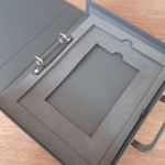 Open grey handled file box with a two-ring binder mechanism and layered foam insert.