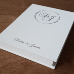 Angled view of a white linen-wrapped invitation box with silver foil lettering.