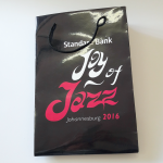 High-gloss black paper bag with full-color logo printing and a single black cord handle