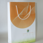 White and orange matte-finish paper bag with white rope handles and a government crest.