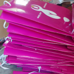 Stack of magenta high-gloss paper bags with white cord handles and branding