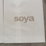 Close-up of a white paper sandwich bag featuring a minimalist tan silkscreened logo.