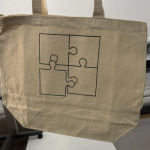 Natural canvas tote bag featuring a black silkscreened puzzle-piece line art illustration.