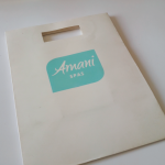 White card bag featuring a die-cut slit handle and a teal Pantone-matched silkscreened logo.