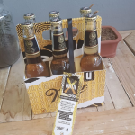 Custom-printed cardboard carry box holding six glass bottles with an attached marketing tag.