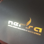 High-shine gold foil logo on a matte black rigid substrate.