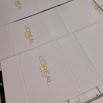 Branded white rigid box flats undergoing a gold silk-screening process.